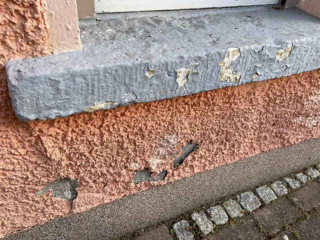 Damp and spalled plaster at the base of an external wall in a rented flat